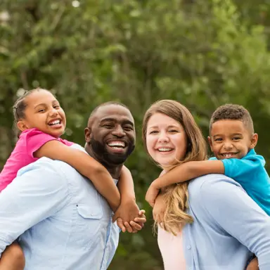 A Black father and white mother posing with their children on their backs, smiling at the camera.