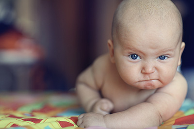 A baby makes a funny expression, perhaps angry or unhappy, but strong.