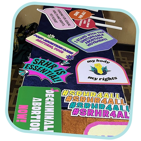 Colorful photo booth props from Oxfam International’s workshop that showcased the sexual health empowerment work from international youth activists. The props read things like, “SRHR is essential!” “Decriminalize abortion now!” “Funding for sexual health and rights, yes please!” “My body, my rights” and “Youth Power”.