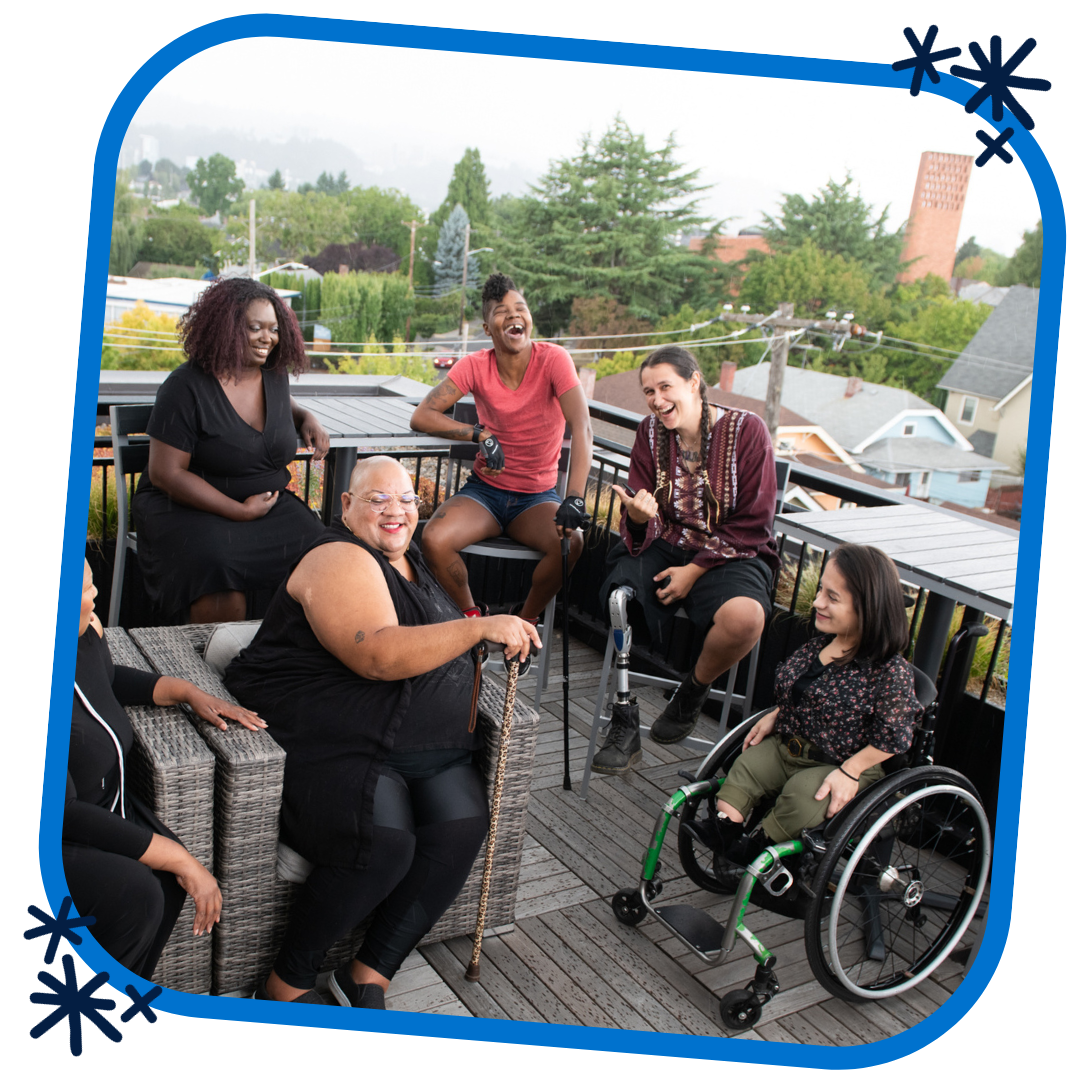 This is a picture in a blue rounded frame with three dark blue asterisks in opposing corners. The picture is an overhead shot of six disabled people of color at a rooftop deck party. An Indigenous Two-Spirit person with a prosthetic leg smiles directly at the camera and gives a thumbs up while everyone else is engaged in conversation.