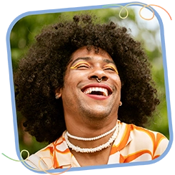 This is a photo of a smiling person with curly hair outdoors in a light blue frame. Around the light blue rounded frame on opposite corners are gradient color squiggles that fade from pink to yellow to green. 