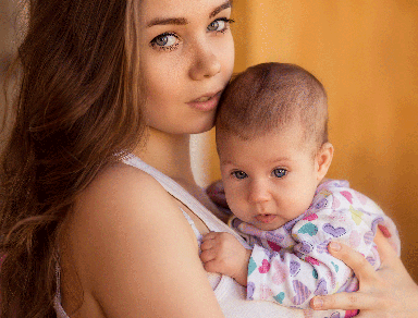 A young white woman holding a baby and looking at the camera.