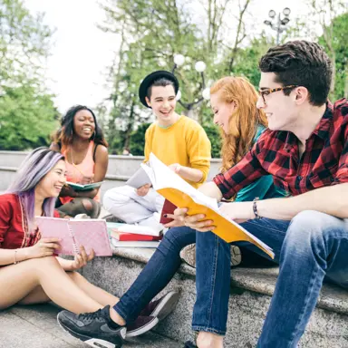 A group of young people study and laugh together outside.